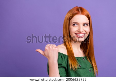 Photo of sweet pretty young lady wear green blouse pointing back looking empty space smiling isolated purple color background