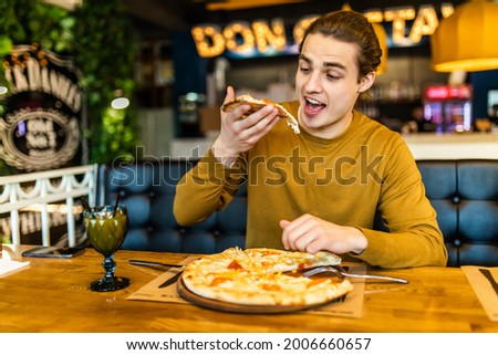 Young happy man eating pizza in cafe