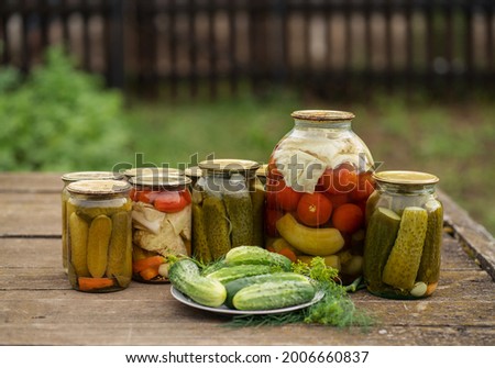 Glass jars with pickles and tomatoes on a wooden table in a rustic style. Plate with fresh cucumbers and dill. Royalty-Free Stock Photo #2006660837