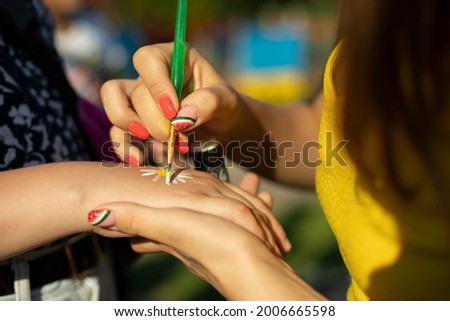 Draws a flower on her hand. The girl draws a flower to the child. Application of paint with a brush.