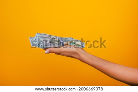 Close up photo of beautiful female hands holding the bunch of dollars of USA isolated on yellow background. Economy, business and finance concept