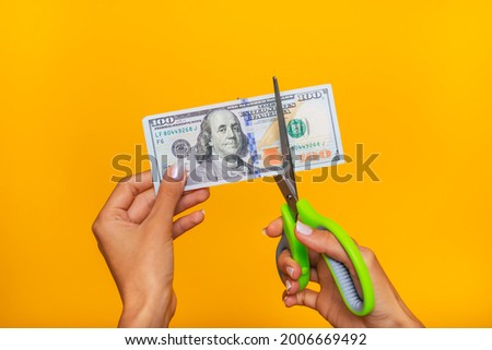 Close up photo of young human hands while cutting one hundred dollars with help of scissors