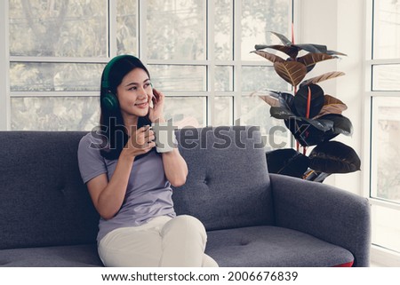 Beautiful asian woman smiling face using smartphone and holding a cup of coffee or tea in hand, Work from home and relaxing time in living room, Lifestyle of people use social media concept.