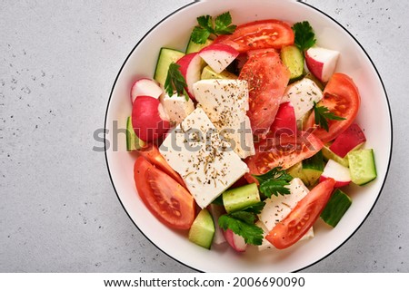 Radish, cucumber, tomato, pepper and feta cheese with spices pepper and olive oil in white bowl on grey slate, stone or concrete background. Healthy food concept. Top view.