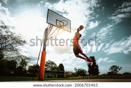 Street basketball player making a powerful slam dunk on the court - Athletic male training outdoor at sunset - Sport and competition concept