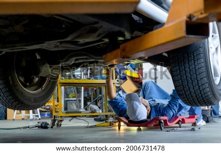 Lower view under car garage worker or technician lie down and check problem in workplace area. Garage management system support employee for working with happiness concept. Royalty-Free Stock Photo #2006731478
