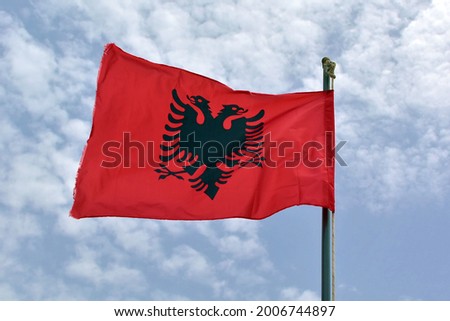 Albania national flag waving in wind on background of blue cloudy sky Royalty-Free Stock Photo #2006744897