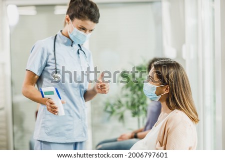 Young pregnant woman with a face mask having her temperature checked before gynecologist check up.