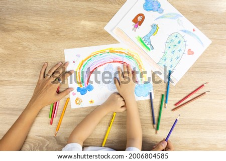 Top view shot of mother and daughter are drawing and coloring beautiful rainbow picture on paper together shows concept of art playing which enhance creativity, learning and enjoyment for child.