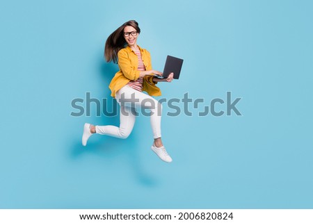 Full body profile side photo of young woman happy positive smile jump up go run hold laptop isolated over blue color background