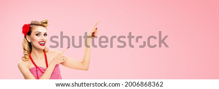 Image of amazed happy woman pointing advertising something. Excited girl in pin up, showing product or copy space for ad text. Retro fashion and vintage. Isolated over rose pink colour background. 