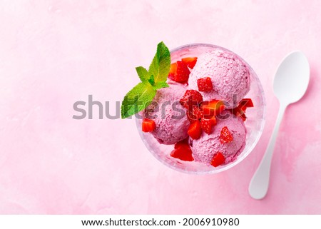 Ice cream sundae with strawberry in a glass bowl on pink background. Copy space. Top view.