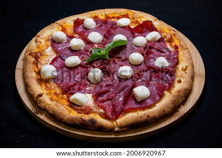 Pizza with tomato sauce, mozzarella and smoked ham on a black background.