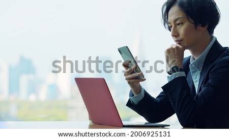 Asian businessman using a smart phone and a laptop PC in the office.