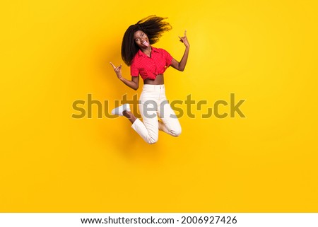 Full size photo of young funky funny crazy afro woman jumping showing tongue rock'n'roll sign isolated on yellow color background