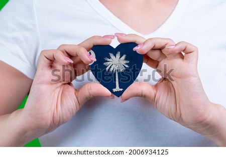 Woman in white t-shirt holds a heart in the form flag South Carolina on her chest. Photo for a postcard on Flag Day, Independence Day, travel, patriotism, other holiday