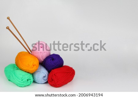 A lot of multi-colored wool balls made of wool yarn lie in the form of a pyramid, bamboo needles close-up on a white background.Handmade concept, needlework, sale of yarn for hobbies.Copyspace.