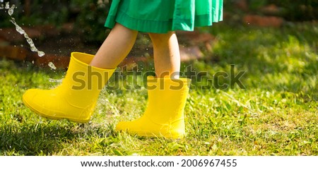 A child in bright yellow rubber boots runs through the puddles. Image with selective focus
