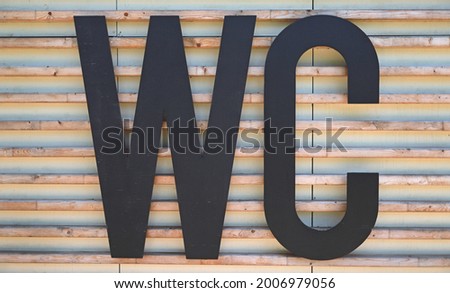 WC sign on the wall. Public toilet symbol. Black lavatory symbol on a wall of wooden paneling in a city park. Public toilet