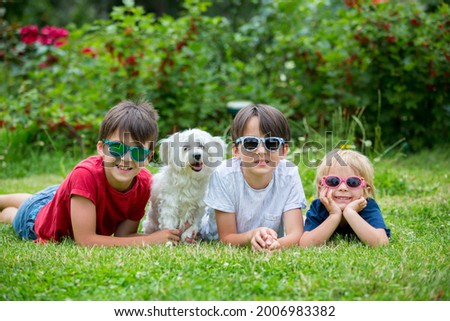 Three children and cute white puppy pet dog with sunglasses, having fun in garden, summertime