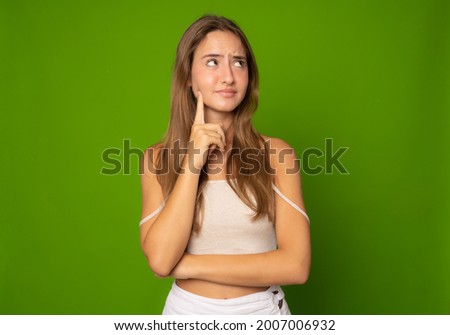 Portrait of a pensive casual girl looking away at copy space isolated over green background
