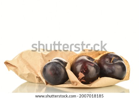 Three dark blue organic plums with a package of paper, close-up, isolated on white.