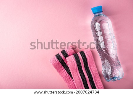 Fitness elastic band ant bottle of water on pink background.