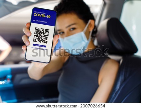 Woman in car wears face mask show screen of smartphone with Covid-19 or coronavirus health passport vaccinated status and QR code sign to show she already get vaccine. Herd immunity concept.