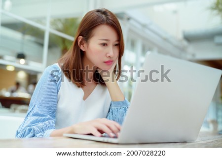 Portrait , a beautiful white Asian woman in a white shirt, sits in front of a computer with an unhappy expression on her face working in a bakery.