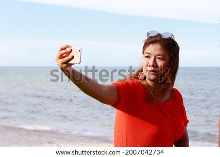 Portrait of young asian women at beautiful beach. Travel on vacation in summer season. One girl use cellphone to selfie, enjoy on holidays in tropical island.