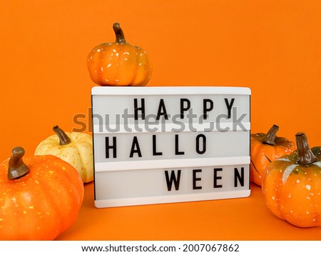Light box with Happy Halloween phrase with pumpkins decoration on orange background.