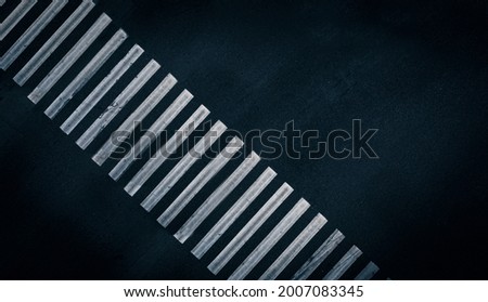 White stripes of paint on empty pedestrian crossing: designation of a pedestrian crossing. An empty pedestrian crossing on the black asphalt road of the street. Aerial top view shot. Road Background. Royalty-Free Stock Photo #2007083345