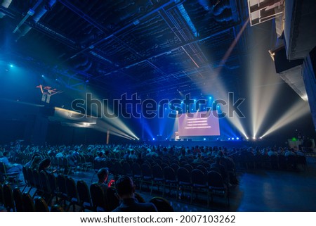 Unrecognizable people sitting on chairs in front of stage with blank screen during business conference in dark hall Royalty-Free Stock Photo #2007103262