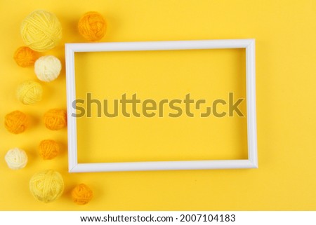 A white empty frame and a lot of yellow balls of yarn of different shades for knitting or crocheting on a yellow background.The concept of manual labor, crafts, hobbies.Top view.Flatlаy.Copyspace