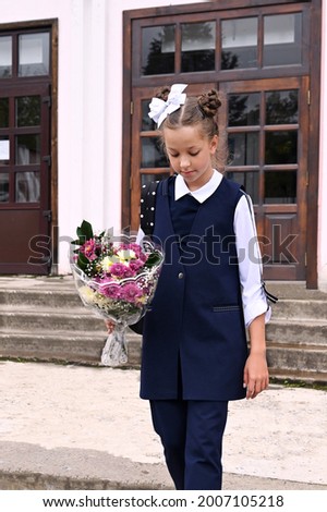 beautiful schoolgirl girl with white bow in her hair and beautiful school uniform with bouquet on the school porch. First day of school. Back to school. Knowledge Day