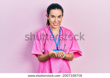 Young brunette woman wearing doctor uniform and stethoscope smiling with hands palms together receiving or giving gesture. hold and protection 