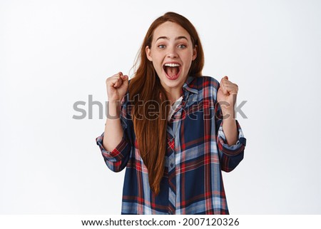 Image of redhead girl screaming with excitement, winning and celebrating, dancing from joy like winner, become champion, standing happy against white background