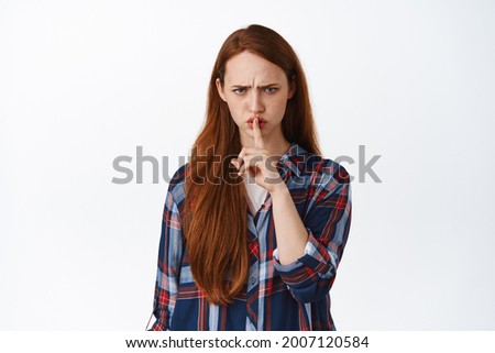 Image of angry ginger girl shushing, say shh and frowning displeased, prohibit, tell to be quiet, hush shut up, dont say anything, standing over white background