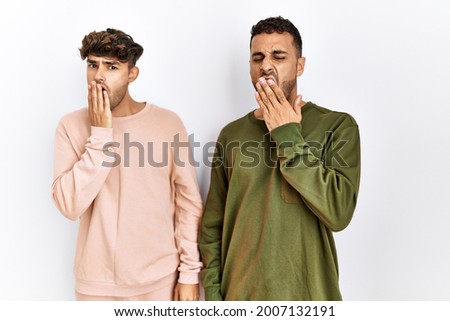 Young gay couple standing over isolated white background bored yawning tired covering mouth with hand. restless and sleepiness. 