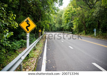 Yellow warning sign winding road with nature