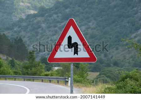 A traffic sign, warning of a double curve next to the road