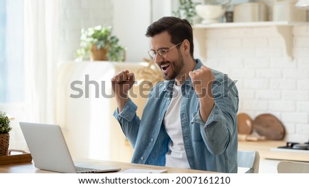 Happy guy celebrate great news opportunity got read by e-mail. Excited man sit in kitchen look at laptop screen with clenched fists feels incredible amazed received good notice. Sale, discount concept Royalty-Free Stock Photo #2007161210