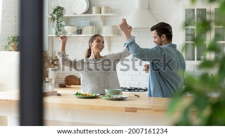 Carefree active millennial couple dancing together in cozy modern kitchen, listening to favourite music raise hands moving enjoy romantic date and happy relocation day to own rented fashionable house Royalty-Free Stock Photo #2007161234