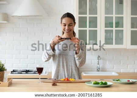 Young woman food blogger standing in kitchen hold smartphone take photo of sliced vegetable salad ingredients to share on social media. Preparation of healthy dinner, record of recipe for vlog concept