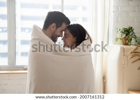Side view millennial beautiful romantic couple awakened together wrapped in blanket standing together in kitchen, enamoured spouses embracing smiling touch foreheads enjoy moment of tender and love Royalty-Free Stock Photo #2007161312