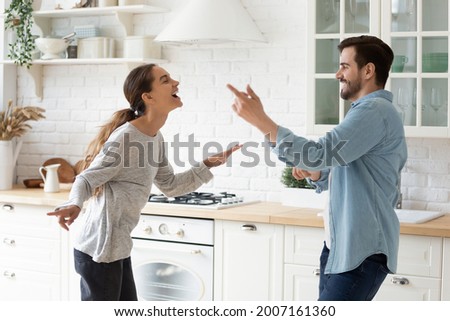 Excited cheery active couple listen music sing dance together at modern renovated home. Happy young spouses enjoy festive mood celebrate relocation day in fashionable cozy kitchen. Hobby, fun concept Royalty-Free Stock Photo #2007161360