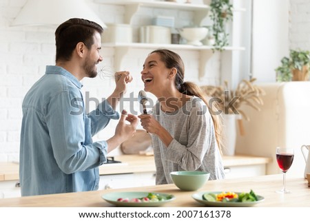 Cheery couple holding kitchenware singing having fun together in kitchen, use whisk and spoon like microphones imagining to be in karaoke enjoy weekend at home. Hobby, happy homeowners family concept Royalty-Free Stock Photo #2007161378