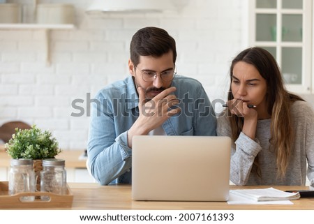 Serious concerned married couple sit indoor looking at laptop read news, receive notification from bank about overspend, financial debt, feel worried, learn new conditions, high rates, taxes concept Royalty-Free Stock Photo #2007161393