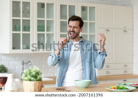 Millennial excited man cooking healthy tasty vegetarian breakfast in kitchen, holds whisk singing having fun, entertaining enjoy good morning new day and favourite pastime. Talent, home hobby concept Royalty-Free Stock Photo #2007161396
