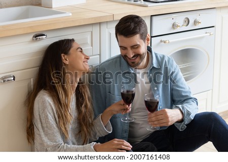 Mixed race couple sit on floor drink red wine relieving fatigue at moving day, celebrate relocation to own house. Romantic dating, kitchen renovation services ad, relations, housewarming event concept Royalty-Free Stock Photo #2007161408